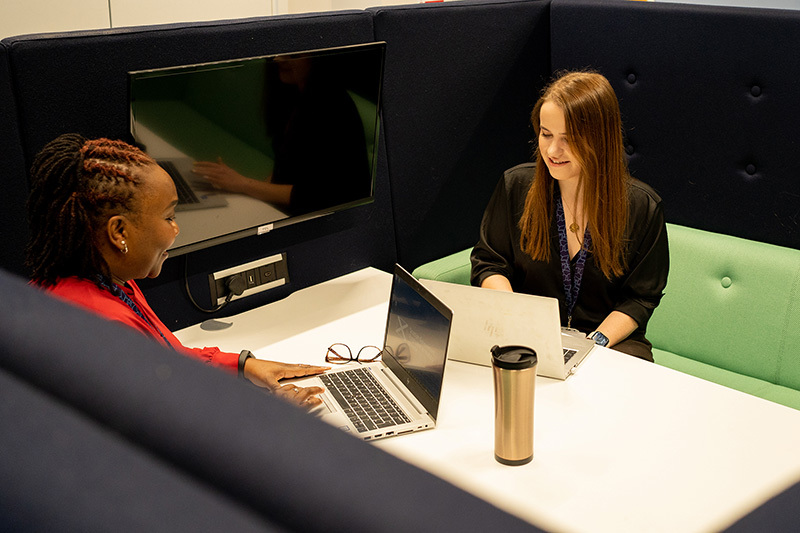 Two women sitting opposite each other. Both are smiling and have laptops in front of them.