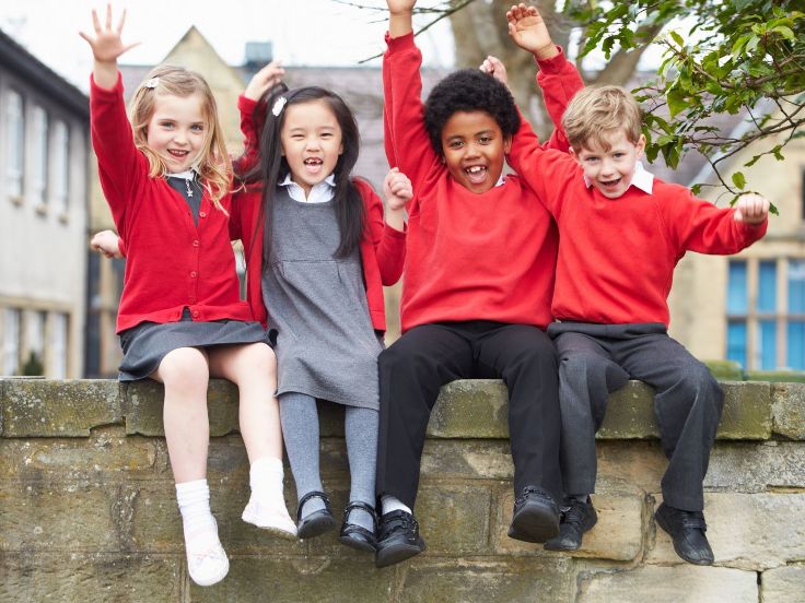 Four children in school uniform sitting on a wall