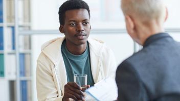 Two people in conversation, one holding a glass of water, the other holding documents.