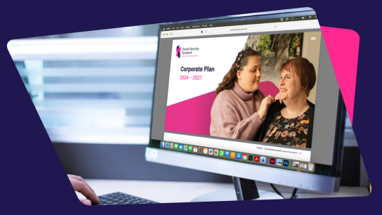Computer monitor displaying Social Security Scotland’s Corporate Plan webpage, with a person’s hand on a keyboard.
