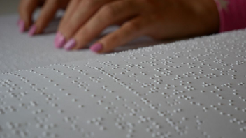 Hands touching textured white paper, possibly reading Braille.