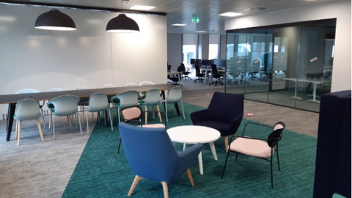 Empty modern office space with tables, chairs, and pendant lights.
