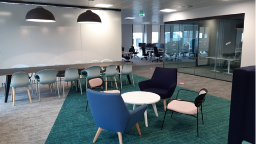 Empty modern office space with tables, chairs, and pendant lights.