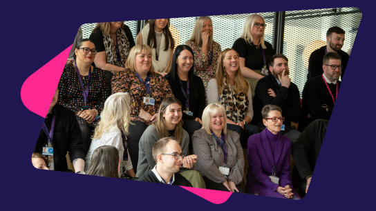 Group of people seated in a tiered arrangement inside a modern office space, wearing business-casual clothing.
