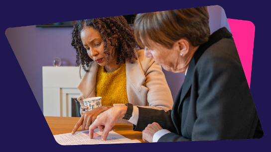 Two people seated at a table, reviewing a document together, with one pointing and the other holding a cup.