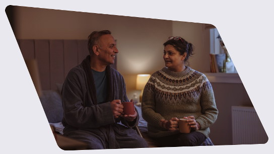 Two people are sitting on a bed looking at each other and smiling
