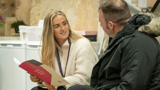 Two individuals in conversation, one holding an open folder with documents.