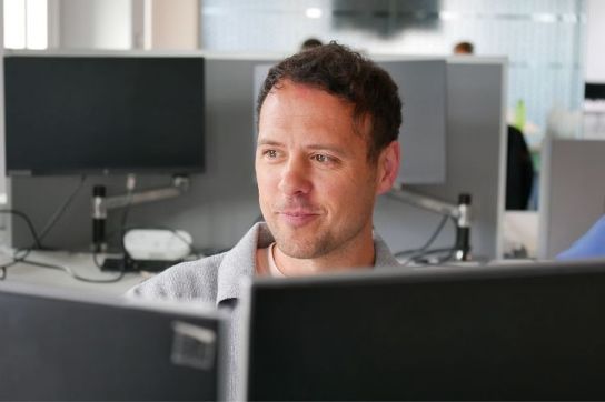 Person seated at a desk, focused on multiple computer screens.