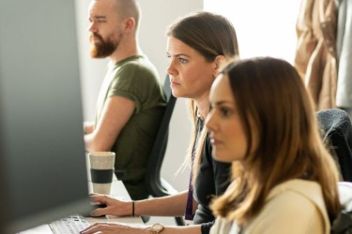 3 people sit at desks working on their computers
