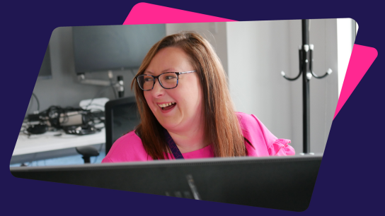 Person seated at a desk in an office, working on a computer monitor.