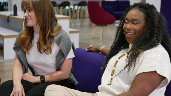 Two people seated on a purple couch in a casual office setting.