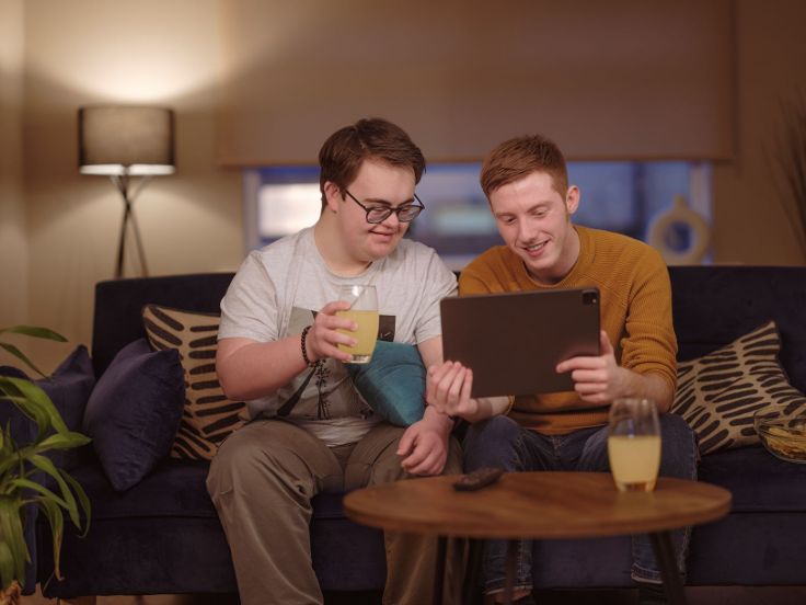 Two people are sitting on a sofa looking at an ipad