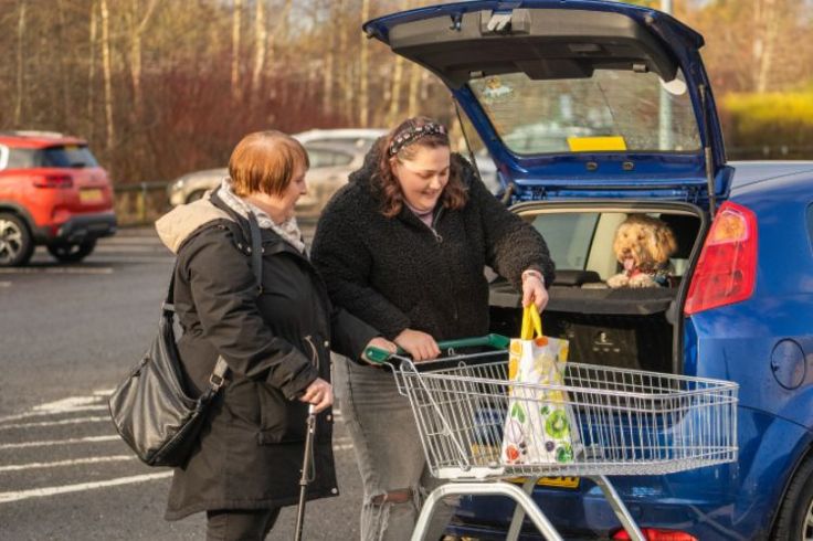 A woman helping to put shopping bags into a car for another woman