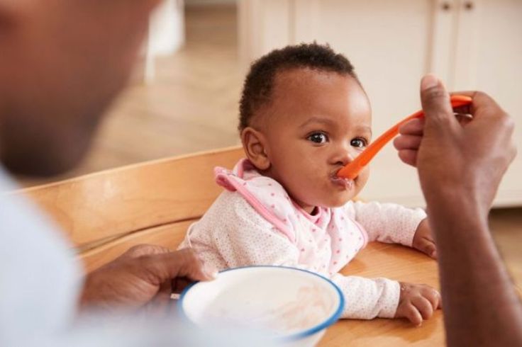 A baby being spoon fed by an adult