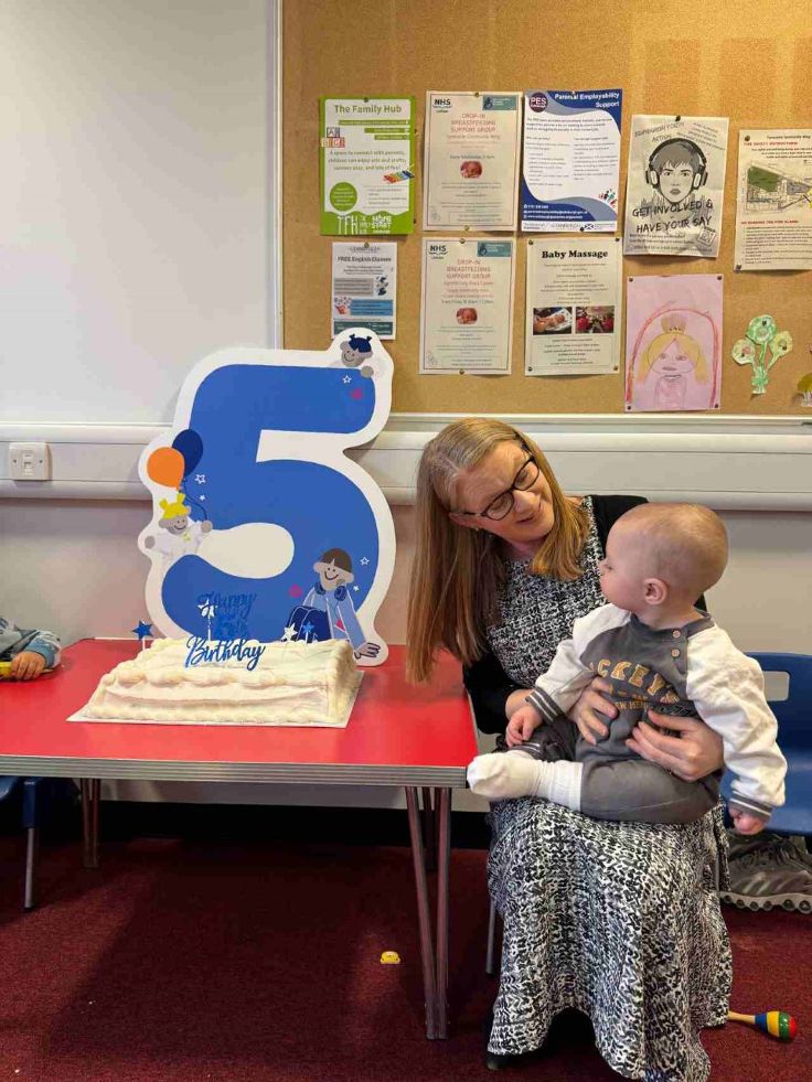 Cabinet Secretary for Social Justice, Shirley-Anne Somerville, holding baby and sitting next to birthday cake