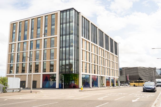 Exterior of Agnes Husband House, Dundee. A modern multi-story building with brick and glass exterior, adjacent to a road