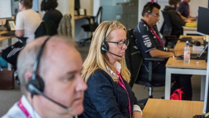 Two colleagues sat at a desk with headsets on