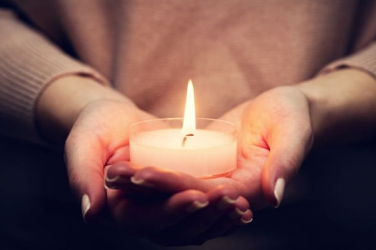 A pair of hands is holding a lit candle