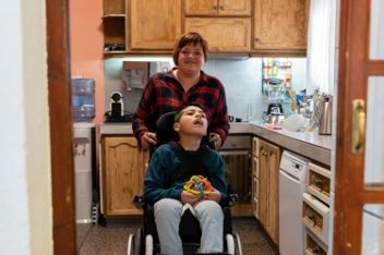 Two people in a kitchen, one standing behind the other in a wheelchair.