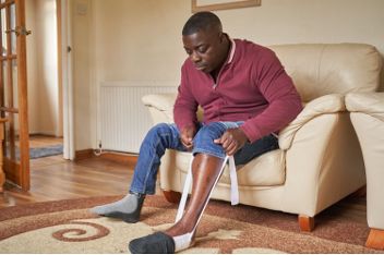 Person seated in a living room, using an aid to put on a sock.