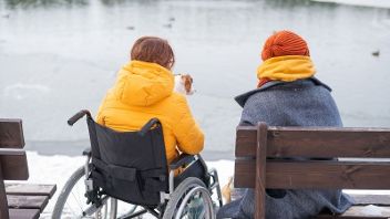 Two people seated by a frozen lake, one in a wheelchair, enjoying the view together.