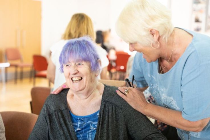 A person has their hands on another person's shoulders. Both are smiling.