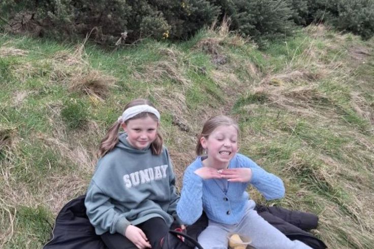 Two girls sat on a grassy verge