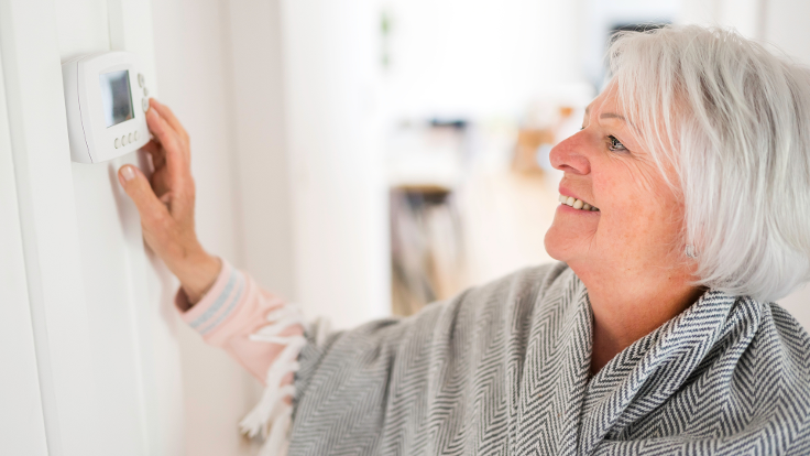 Photograph of an older woman adjusting the thermostat in her home.
