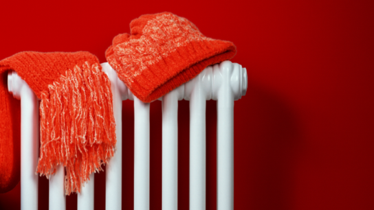 White radiator with a red scarf and hat draped over it against a bright red wall.