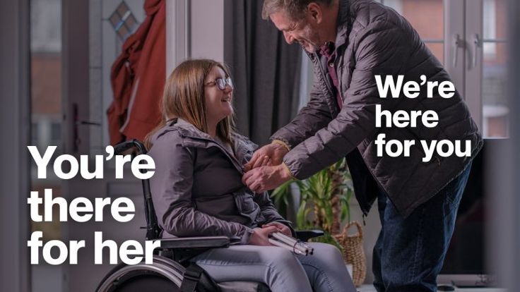 A woman in a wheelchair being helped by a man the caption reads 'You're there for her, we're here for you'