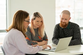 Three people sat around a table looking at a tablet