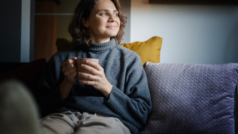 Person sitting on cosy couch with cup of tea.