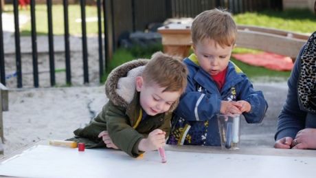 Two young boys drawing on paper outside in a garden