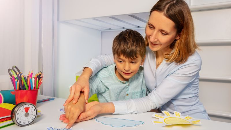 Boy with autism learn weather using cards, teacher hold hands and point to correct one