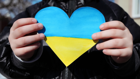 A child is holding a small paper heart in the colours of the Ukrainian flag