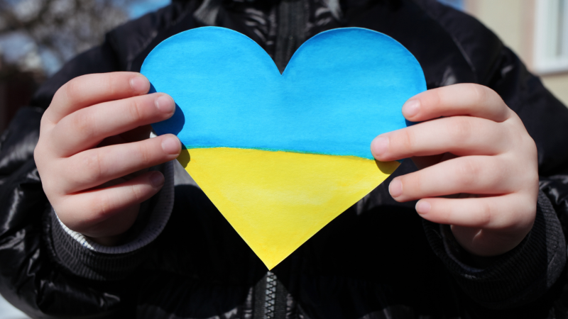 A child is holding a small paper heart in the colours of the Ukrainian flag