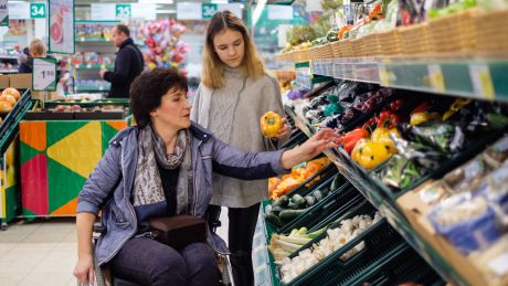Young girl carer helping woman in wheelchair at supermarket