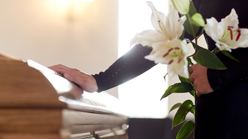 Grieving family member holding a bunch of flowers and resting their hand on a coffin