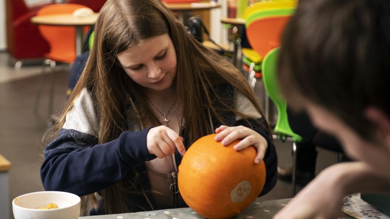 a young carer in a colourful hoodie leans against a worktop within a youth centre.