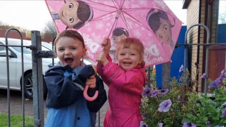 Two young children holding an umbrella and smiling