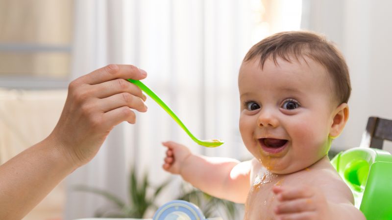 A baby is in a high chair getting fed with a spoon