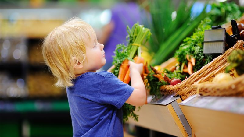 child in supermarket holding carrots