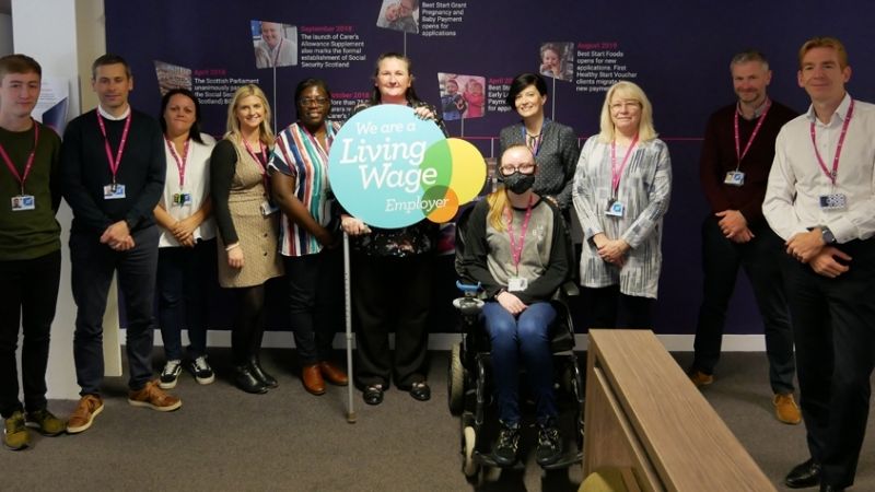 Colleagues stand with a Living Wage Employer sign