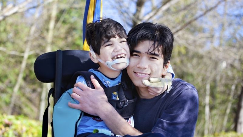 Young carer hugging a young child in a wheelchair