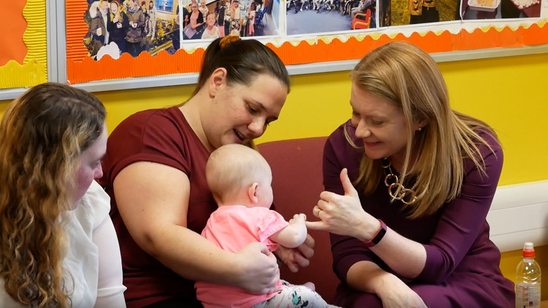 Cabinet Secretary, Shirley Anne Somerville talking to parents and holding hands with a baby