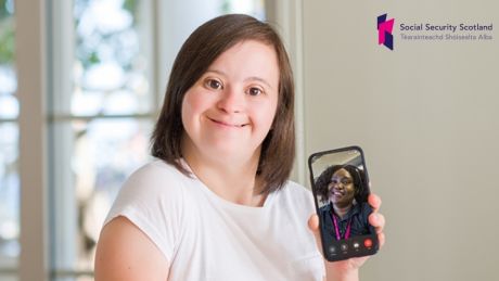 Young woman holding a phone with the face of a client advisor on it