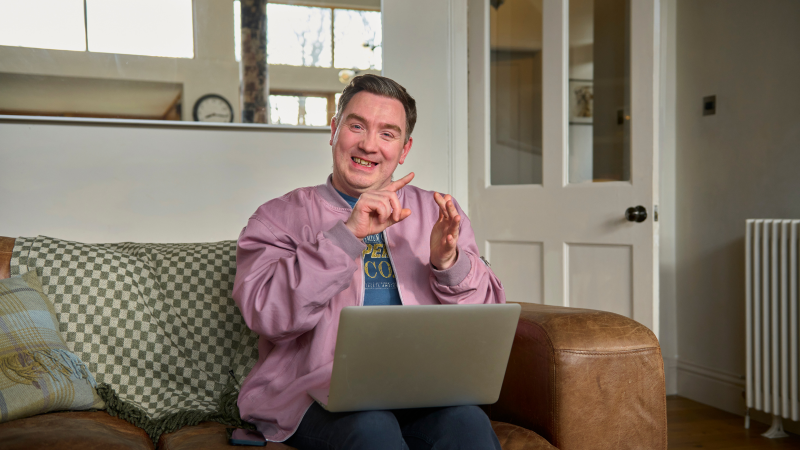 A person is using British Sign Language whilst sitting with a laptop