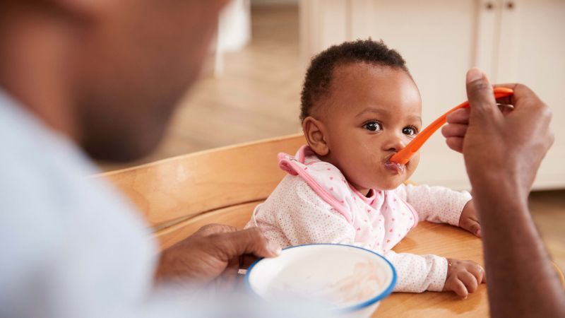 An adult is feeding a baby with a bowl and spoon