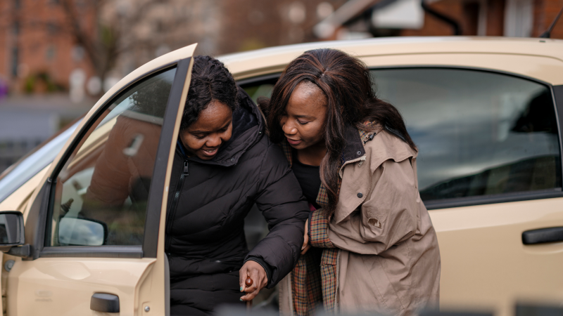 A daughter who is caring for her mother supports her to exit the car