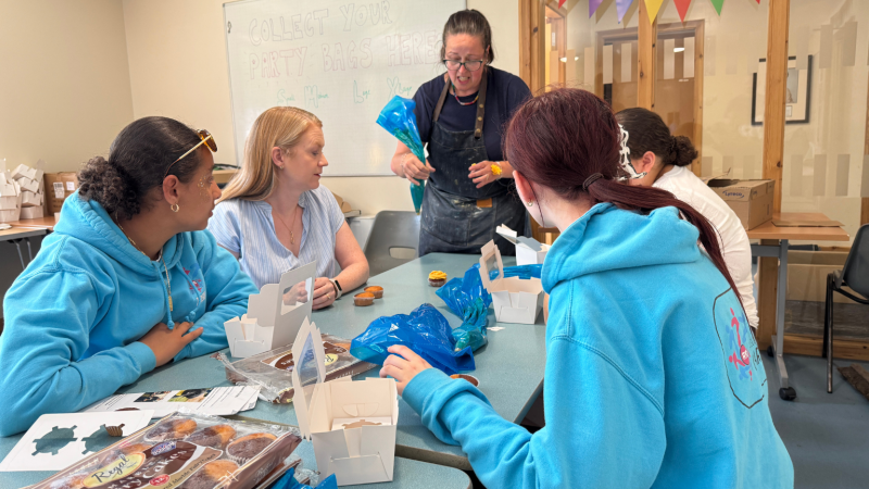 Social Justice Secretary sits with young carers around a table taking part in at a cake decorating activity